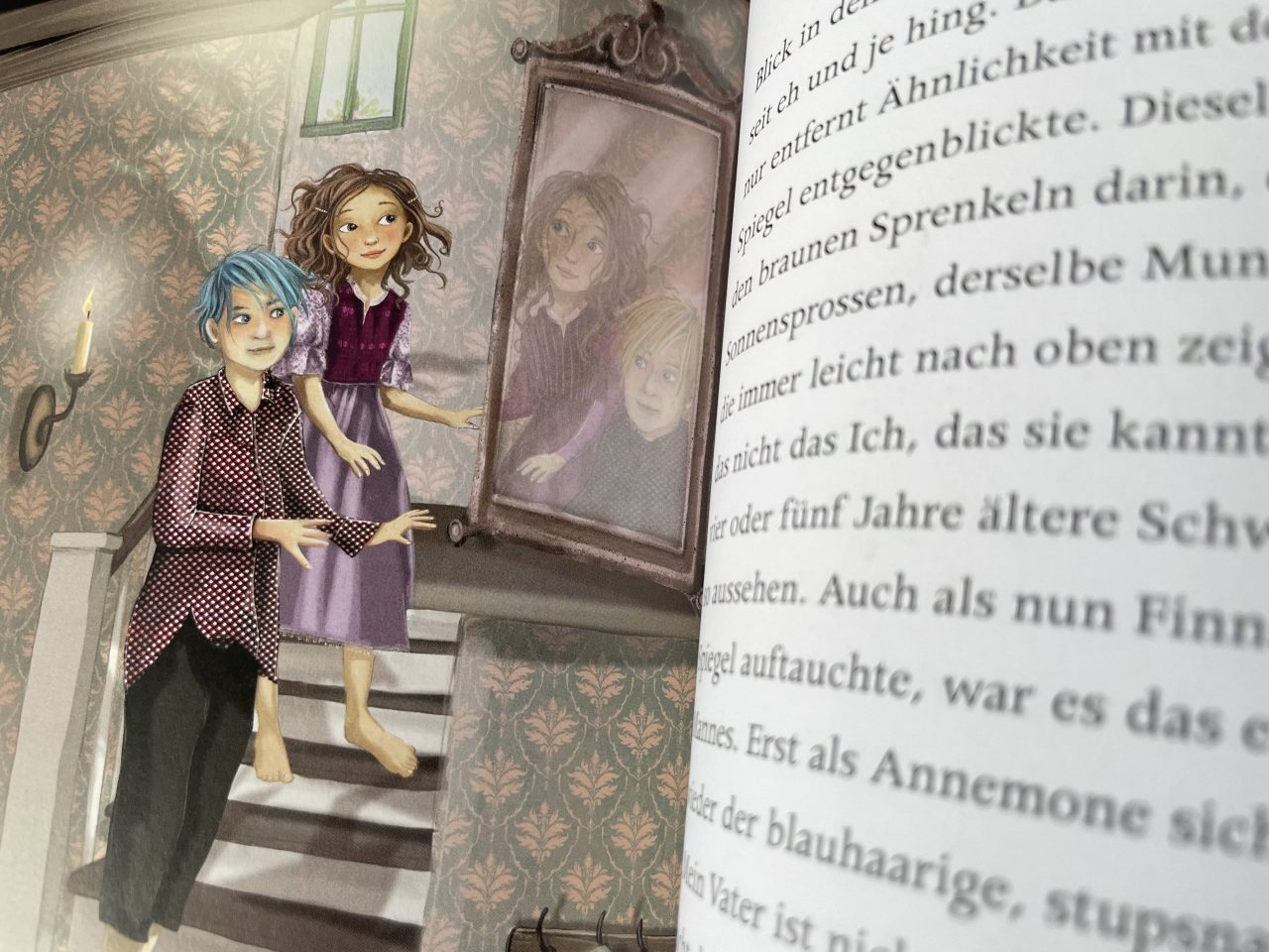 aufgeklapptes Kinderbuch "Annemone Apfelstroh" - links eine Illustration mit zwei Kindern auf einer Treppe, die in einen Spiegel sehen - rechts Text