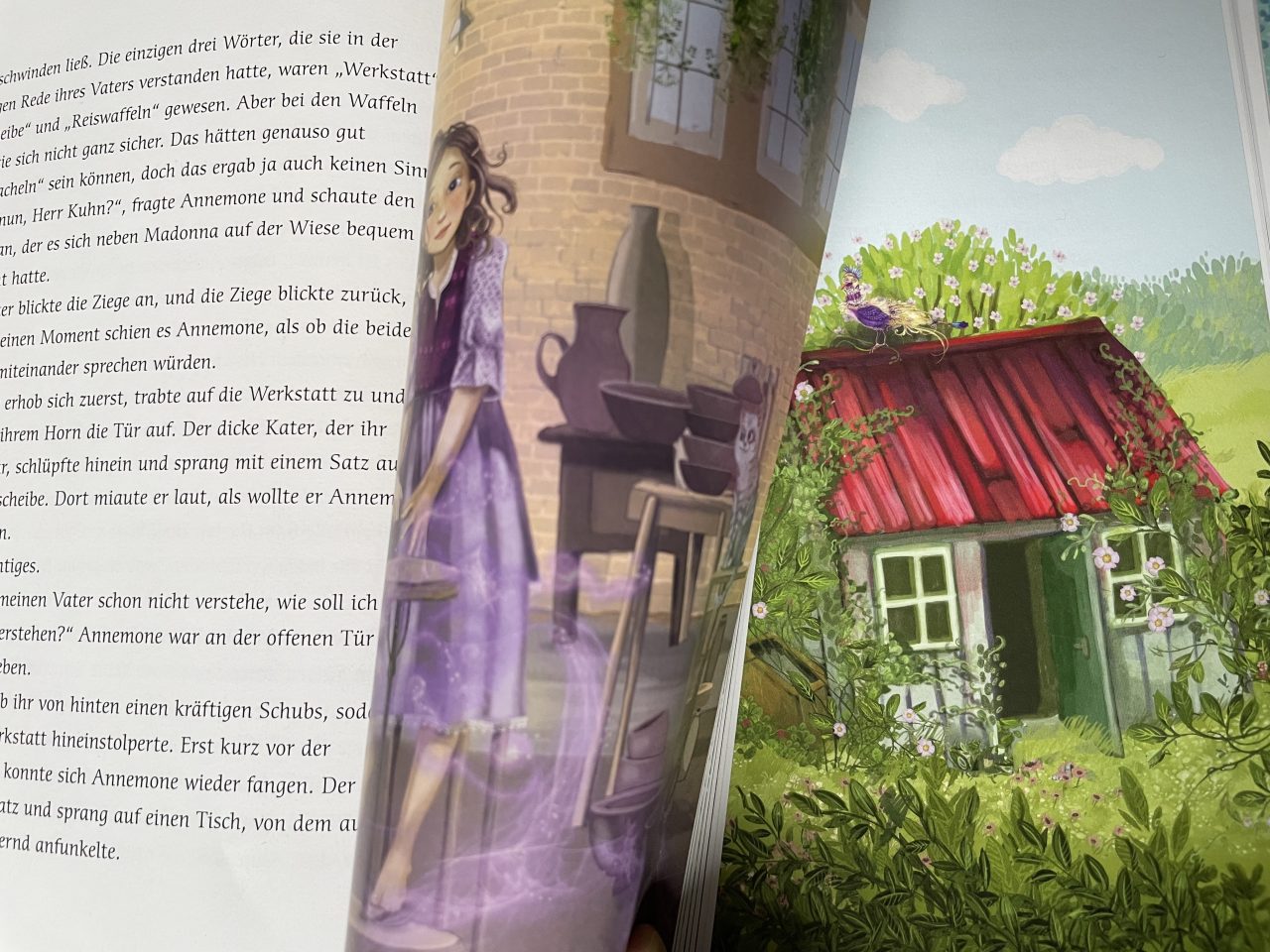 aufgeschlagenes Kinderbuch "Annemone Apfelstroh" mit Text und Illustration - zusehen ist das Mädchen in einer Töpferwerkstatt und ein Häuschen im Grünen 