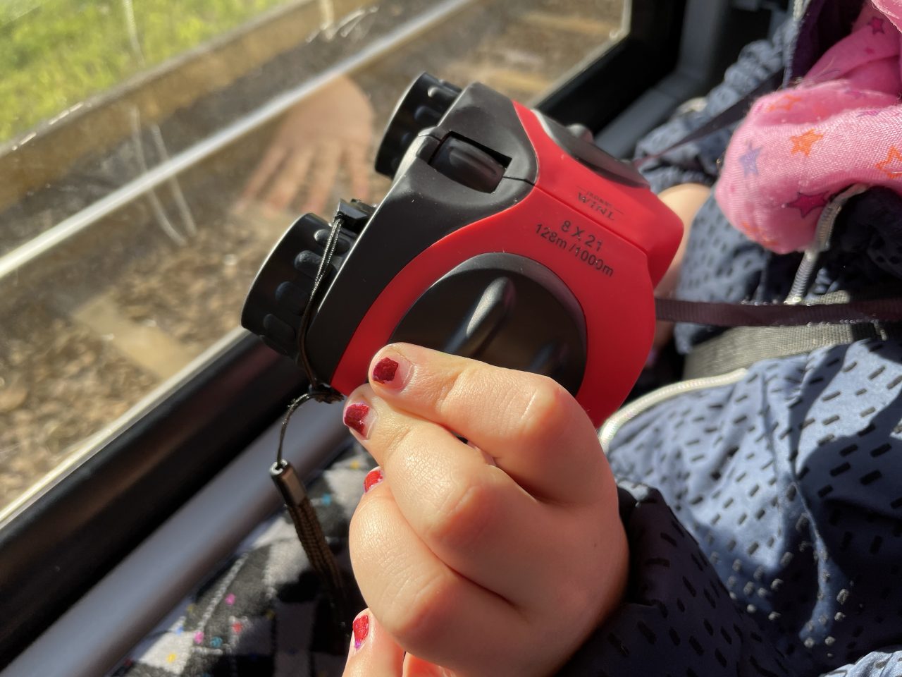 Kinderhand hält ein Fernglas an einem Fenster mit Blick auf die Gleise