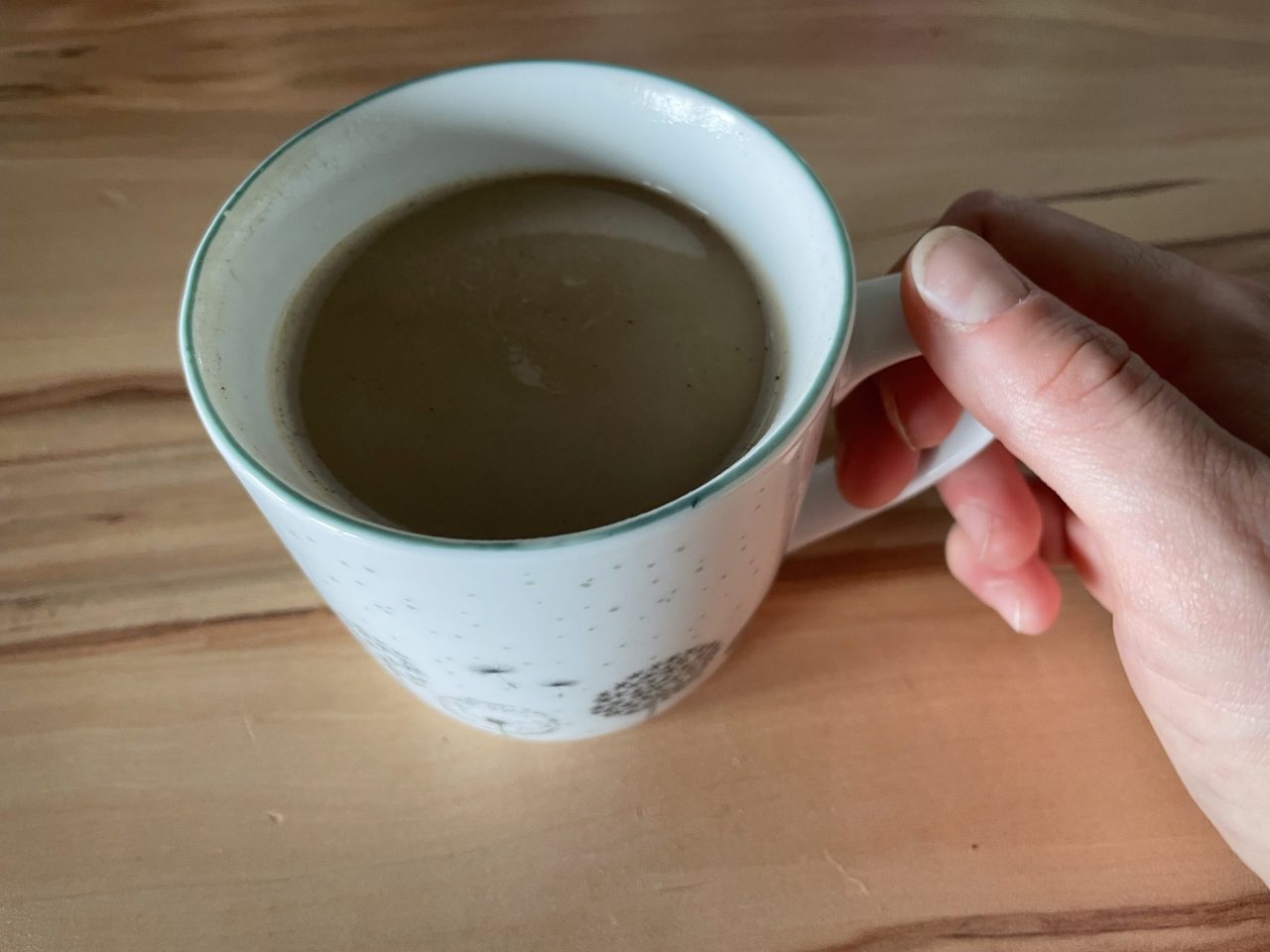 Kaffeetasse mit Inhalt mit einer Hand am Henkel