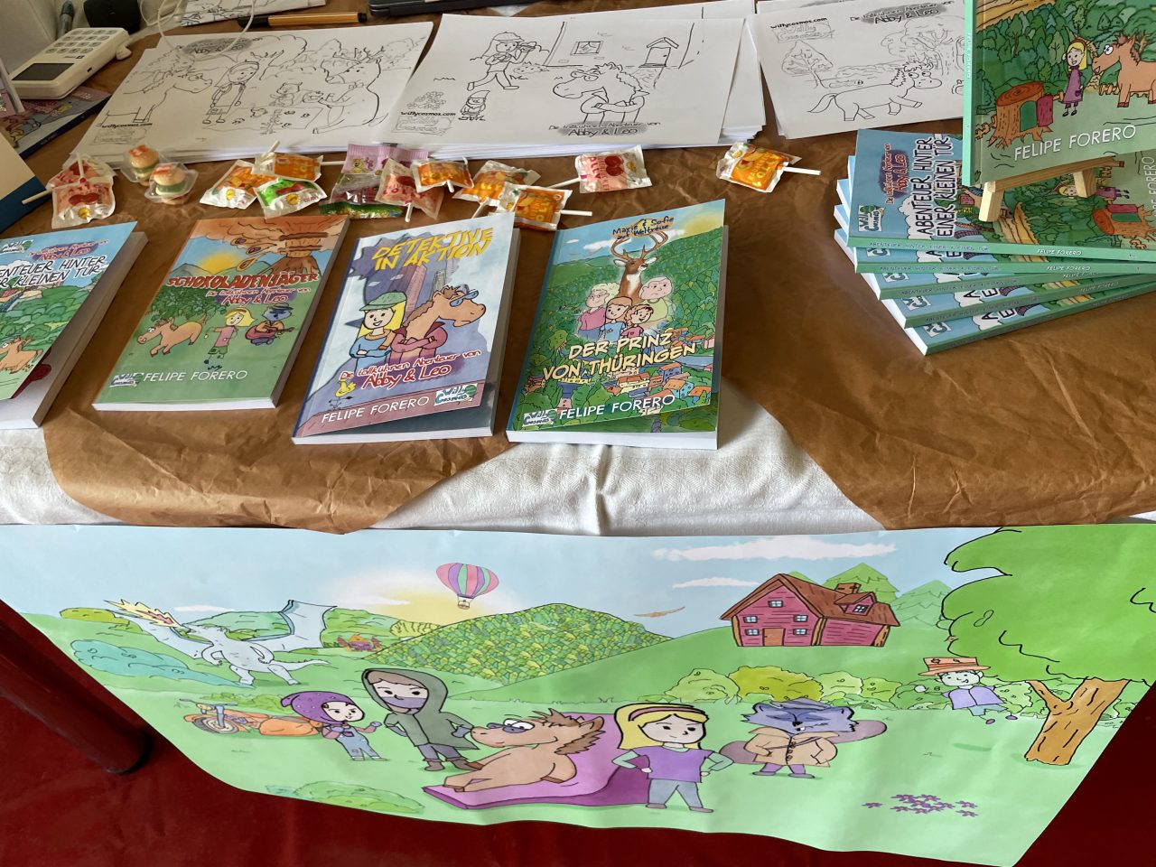 ein Messetisch zur Präsentation von Kinderbüchern mit Plakat davor, Ausgaben und Süßigkeiten