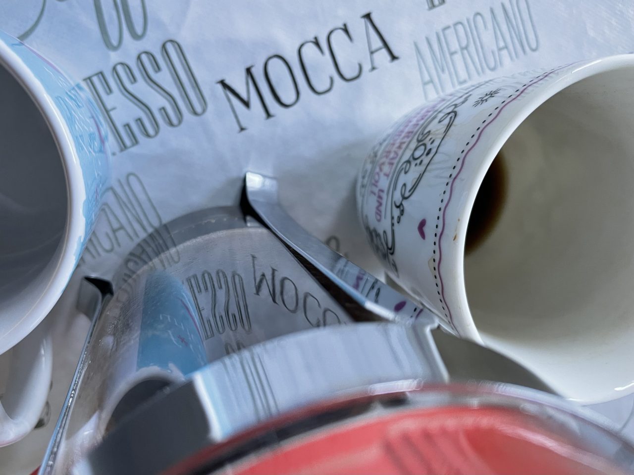 auf einer mit "Mocca" Schriftzügen bedruckten Decke stehen zwei Tassen und eine Kaffeekanne