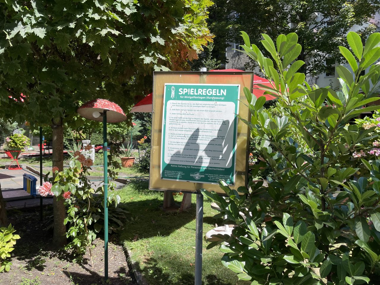 Schild mit Minigolfregeln umgeben von grünen Pflanzen