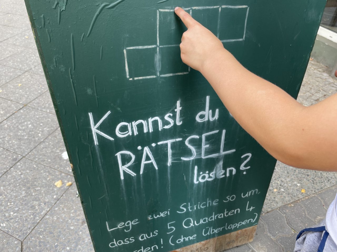 Schild mit einem Rätsel auf der Straße, was von einer Kinderhand berührt wird
