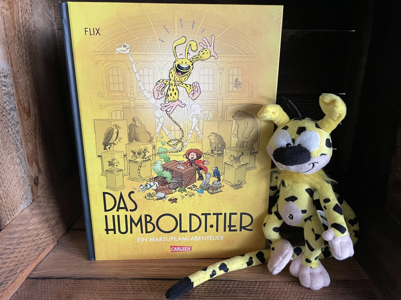 in einer Holzkiste steht das Comicbuch "Das Humboldt-Tier" ein Marsupilami-Abenteuer mit einer Plüschfigur daneben