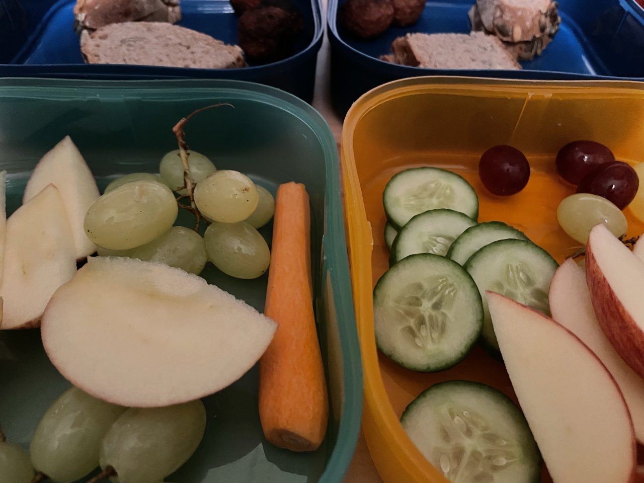 vier Teile von zwei Brotdosen neben und übereinander angeordnet und gefüllt mit Obst, Gemüse und Broten