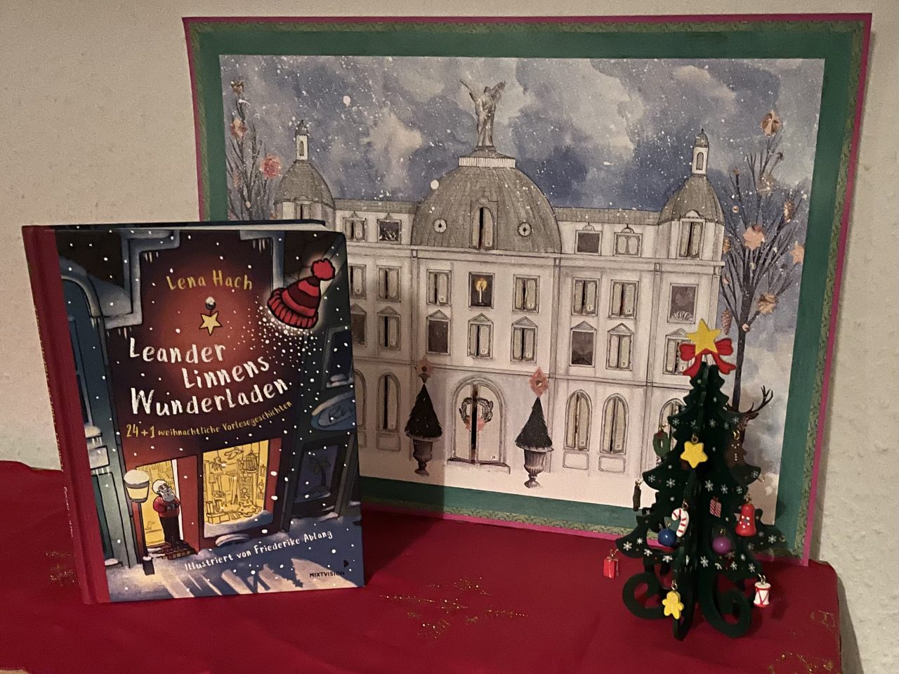 das Adventskalenderbuch "Leander Linnens Wunderladen" steht neben einem Bilderadventskalender "Winterschloss" neben einem kleinen Holzweihnachtsbaum