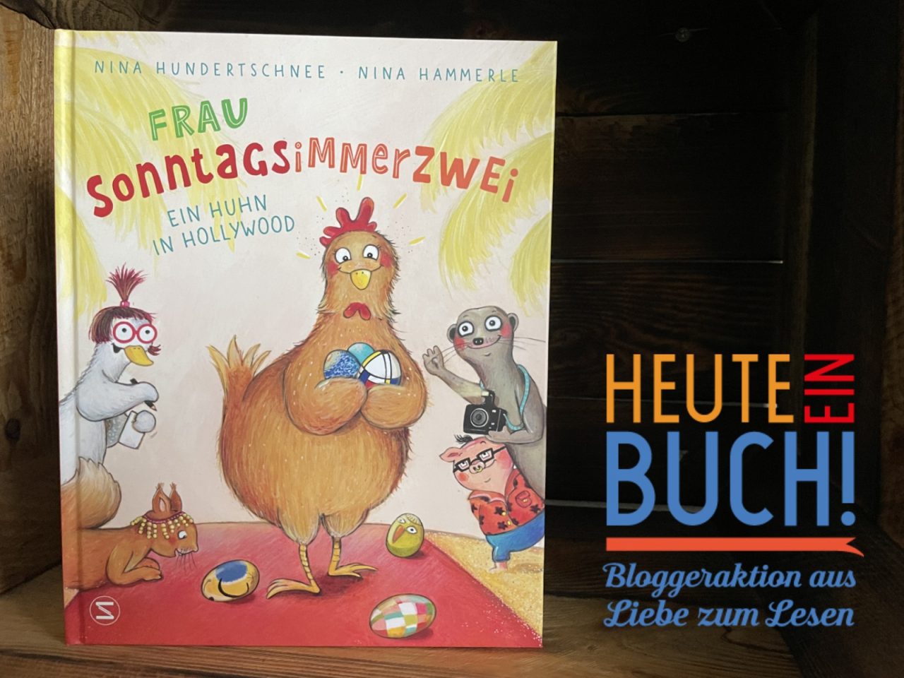 das Bilderbuch "Frau Sonntagsimmerzwei" in einer Holzkiste stehend mit dem "Heute ein Buch"-Logo
