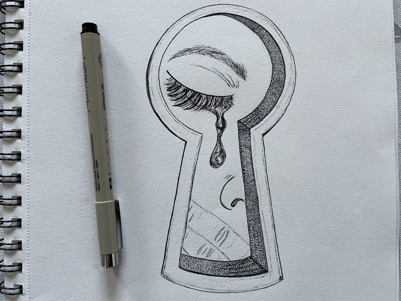 Zeichnung (durchs Schlüsselloch zusehende weinende Person) neben einem Stift 