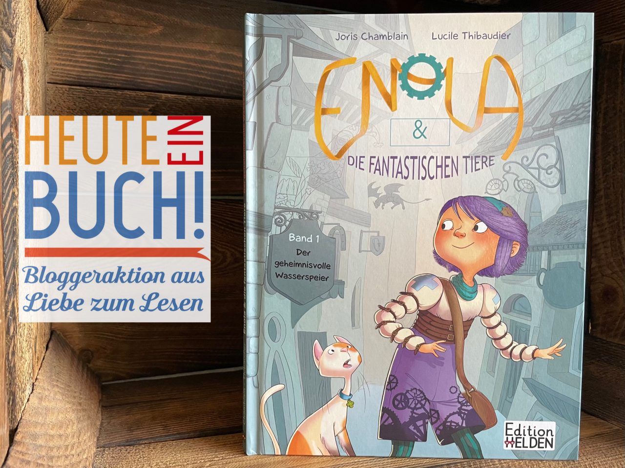 das Kindercomicbuch "Enola & die fantastischen Tiere" in einer Holzkiste stehend mit dem "Heute ein Buch"-Logo