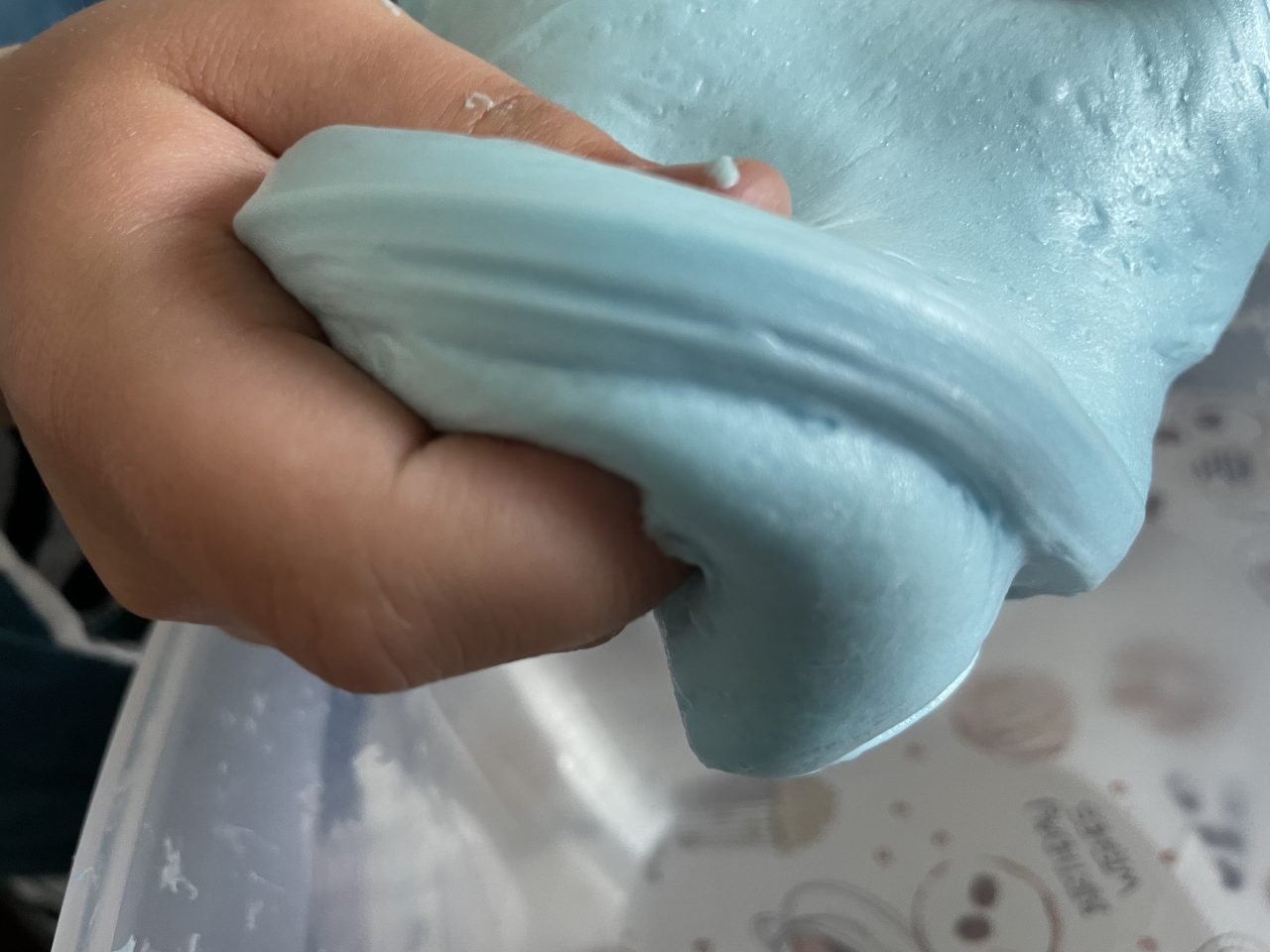 Kinderhand hält hellblauem fluffigem Slime über einer Schüssel