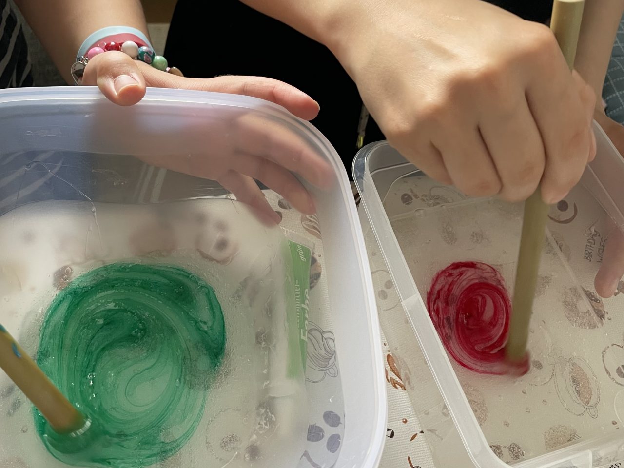 zwei Kinder rühren rote und grüne Farbe in zwei Schüsseln mit durchsichtigem Kleber