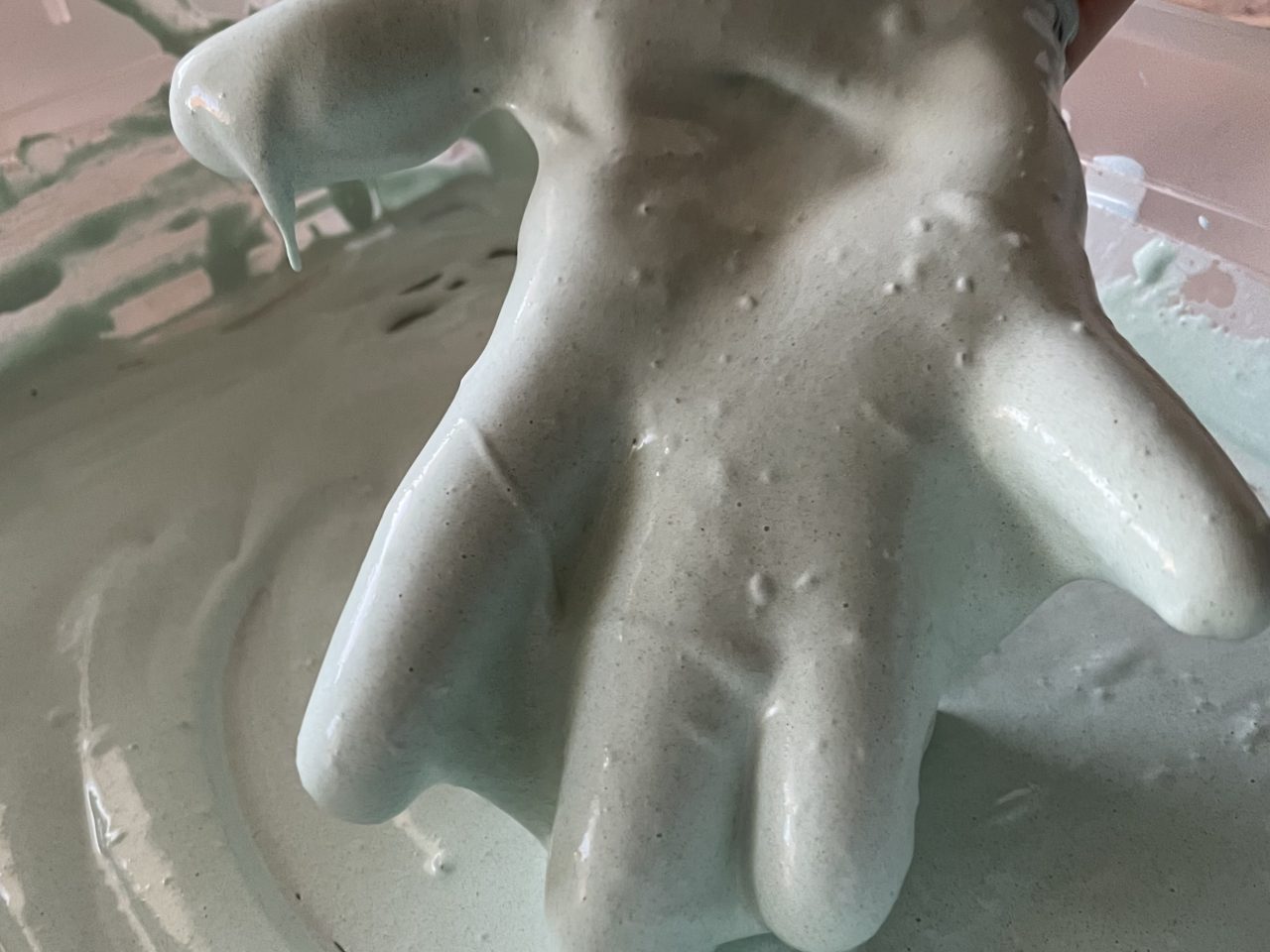 die Hand einer Erwachsenen in flüssigem graugrünen Slime