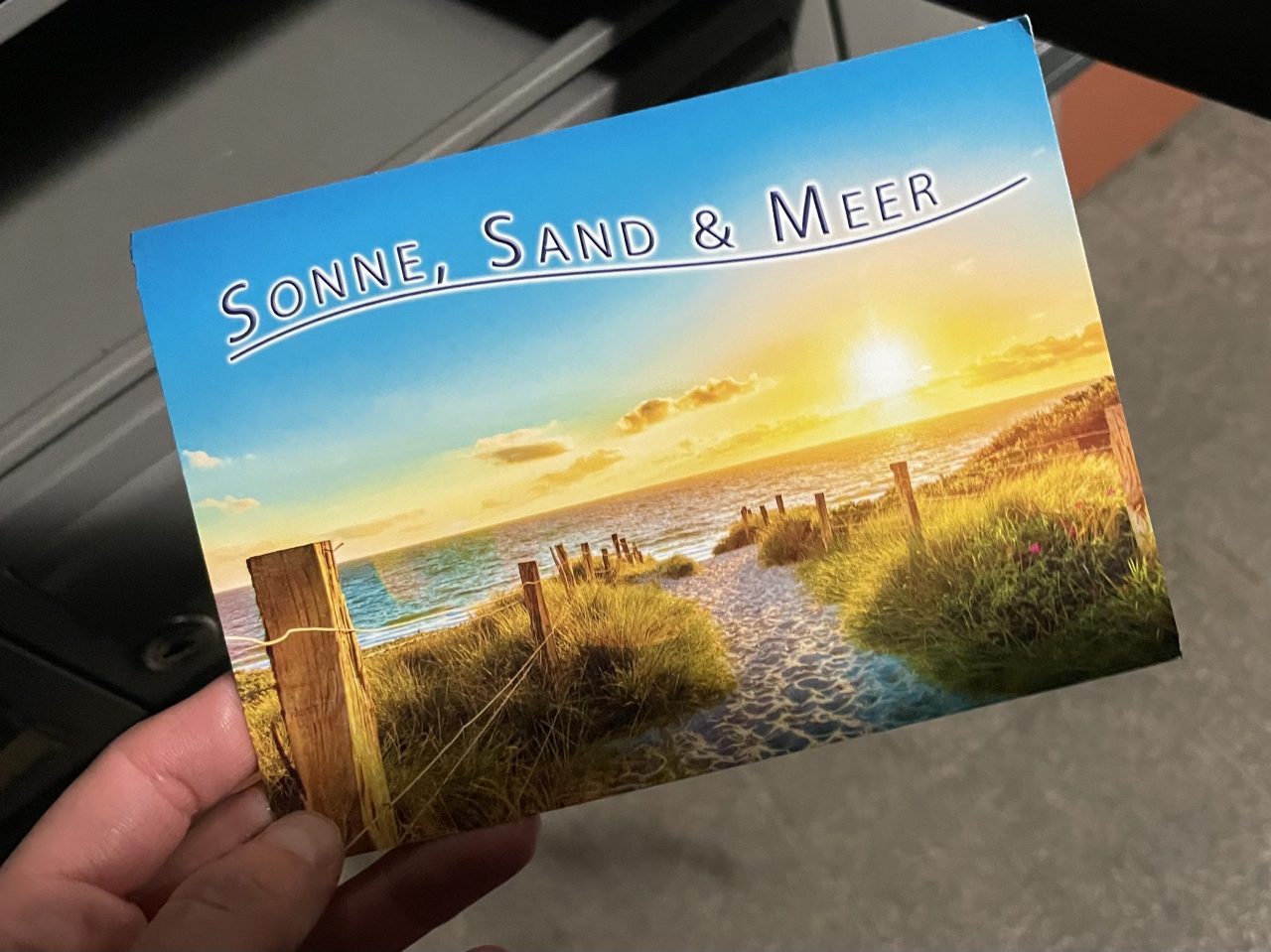 Postkarte mit Seemotiv vor einem Briefkasten gehalten