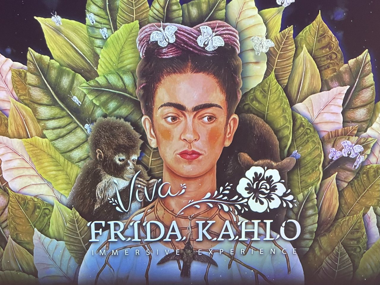 Frida Kahlo - Abbildung mit einem Affen auf jeder Schulter mit Blättern um sich und "Viva Frida Kahlo" - Unterschrift 