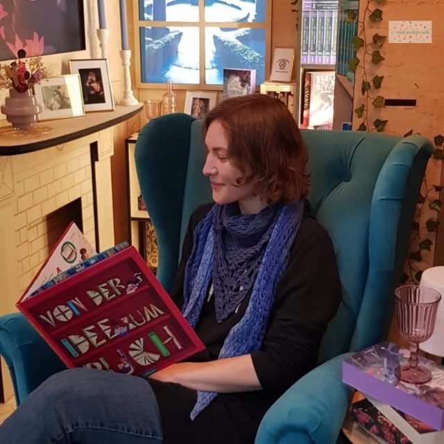 Ich in einem blauen Sessel mit einem Buch am Messestand der Leipziger Buchmesse