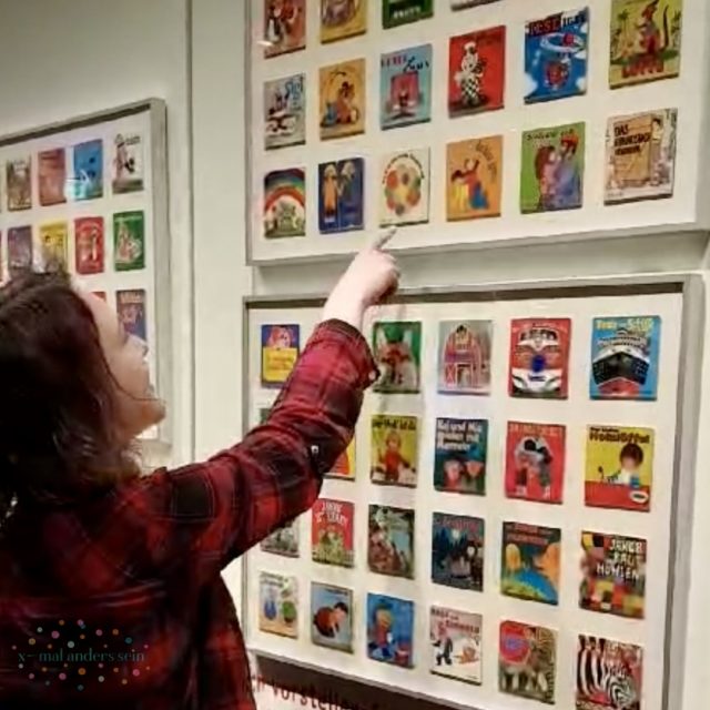 Anne zeigt in der Pixi-Ausstellung auf ein Cover im Rahmen