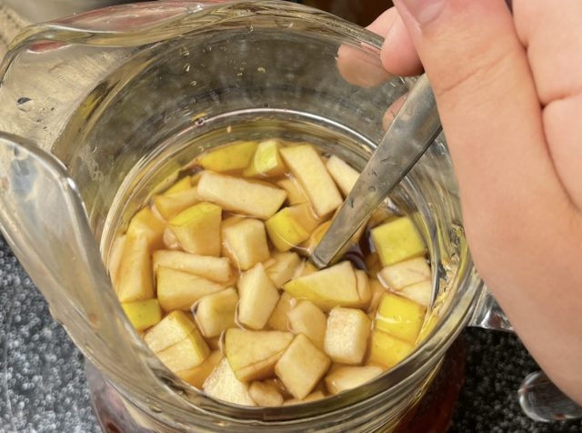 Gefüllter Krug mit kleinen Apfelstückchen mit einem Löffel, den eine Kinderhand hält