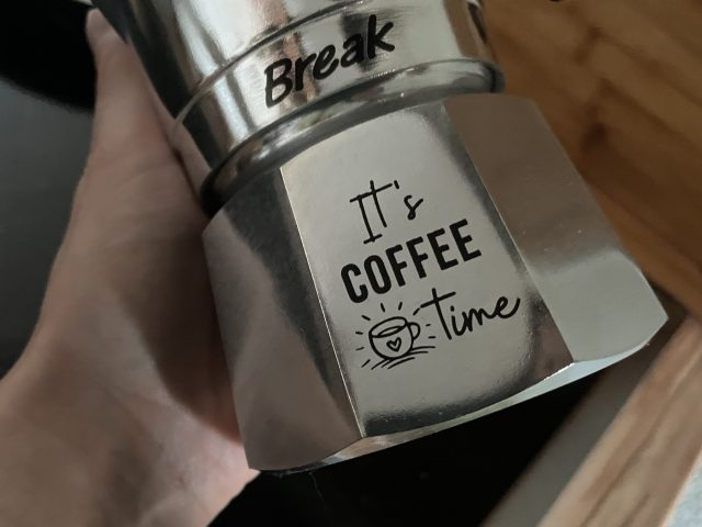 Hand hält einen silbernen Herdkocher mit "It´s COFFEE Time"