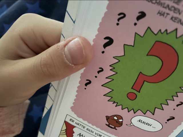 Kinderhand hält einen Comic aufgeschlagen