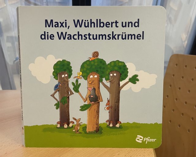 Das aufklärende Kinderbuch "Maxi, Wühlbert und die Wachstumskrümel" auf einem Tisch stehend.