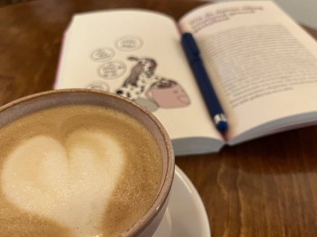 Aufgeschlagenes Buch zum Emotional Load neben einem Kaffe
