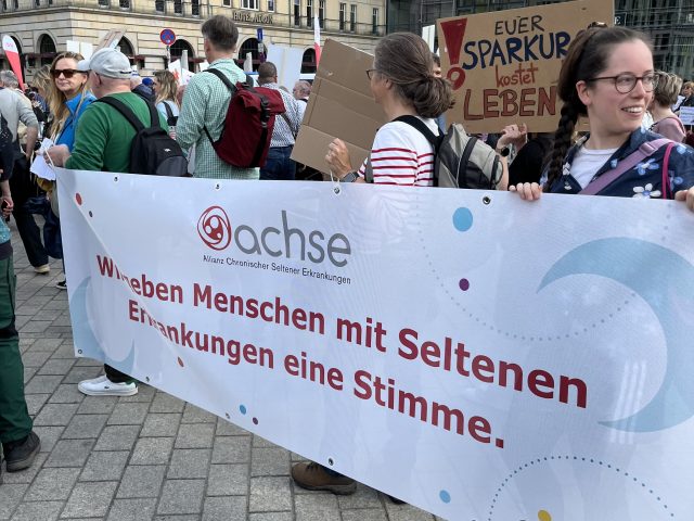 Demonstranten halten ein langes Banner als Stimme für Menschen mit seltenen Erkrankungen